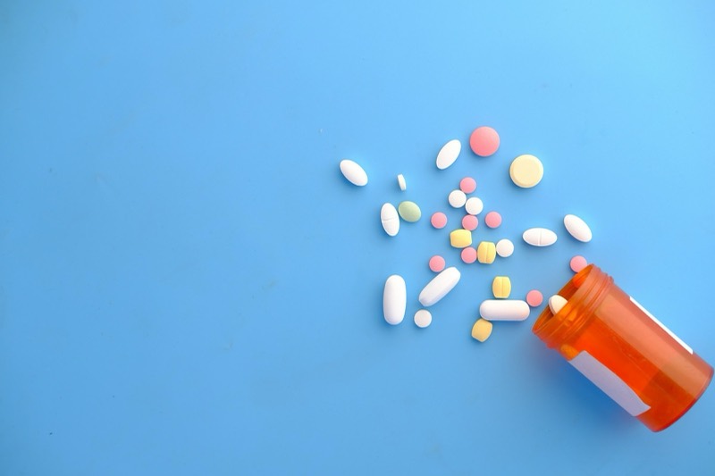 Mixed tablets spilling from an orange pill bottle onto a blue surface
