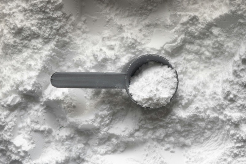 Grey scoop of white powder resting on a bed of white powder