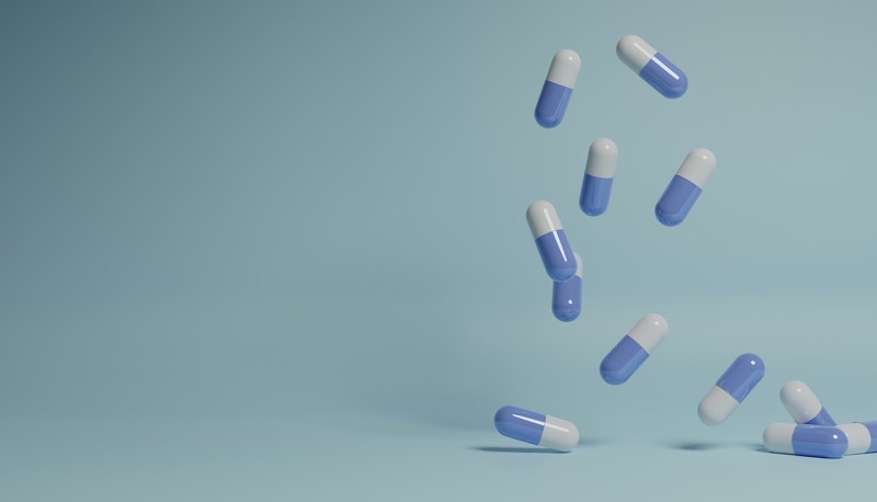Two-tone capsules falling against a plain blue-grey background (3D render)