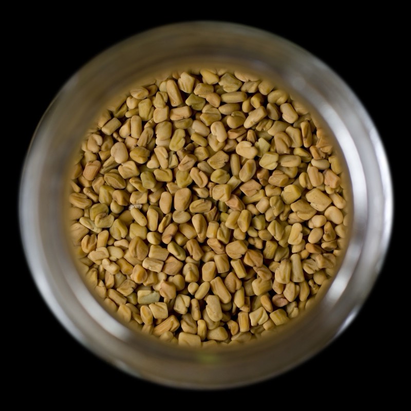 Fenugreek seeds in a glass jar, seen from above on black