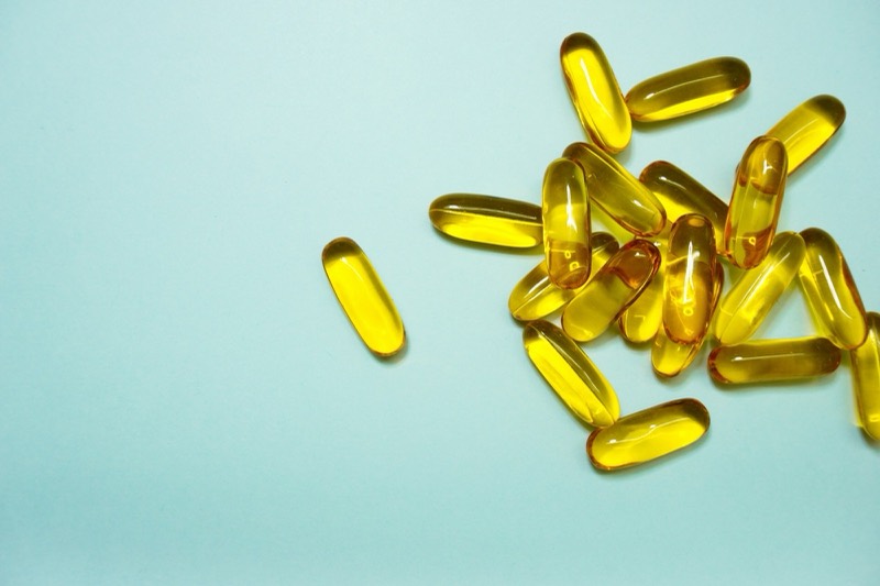 Golden fish-oil softgels on a pale mint background