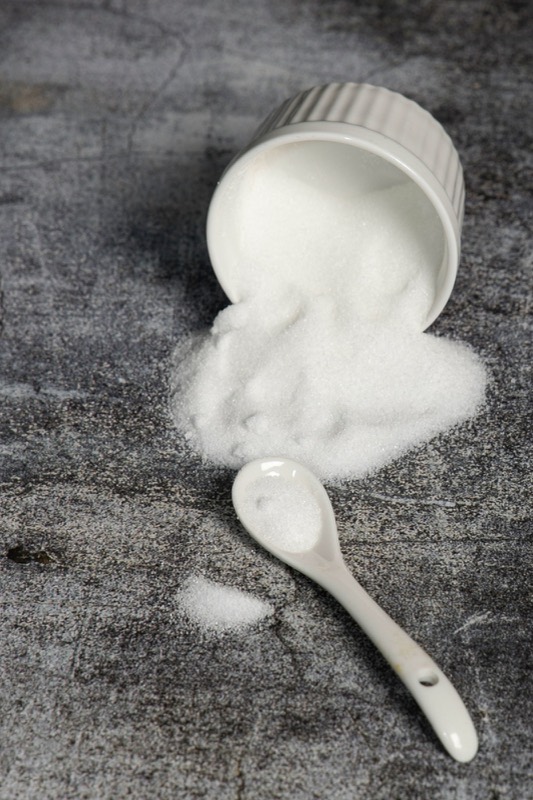 White powder spilling from a ramekin beside a ceramic spoon on grey stone